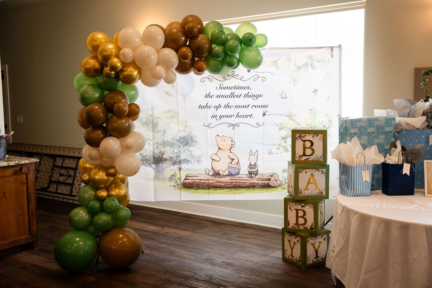 Baby shower setup with green and brown balloon arch and wooden alphabet blocks spelling BABY.