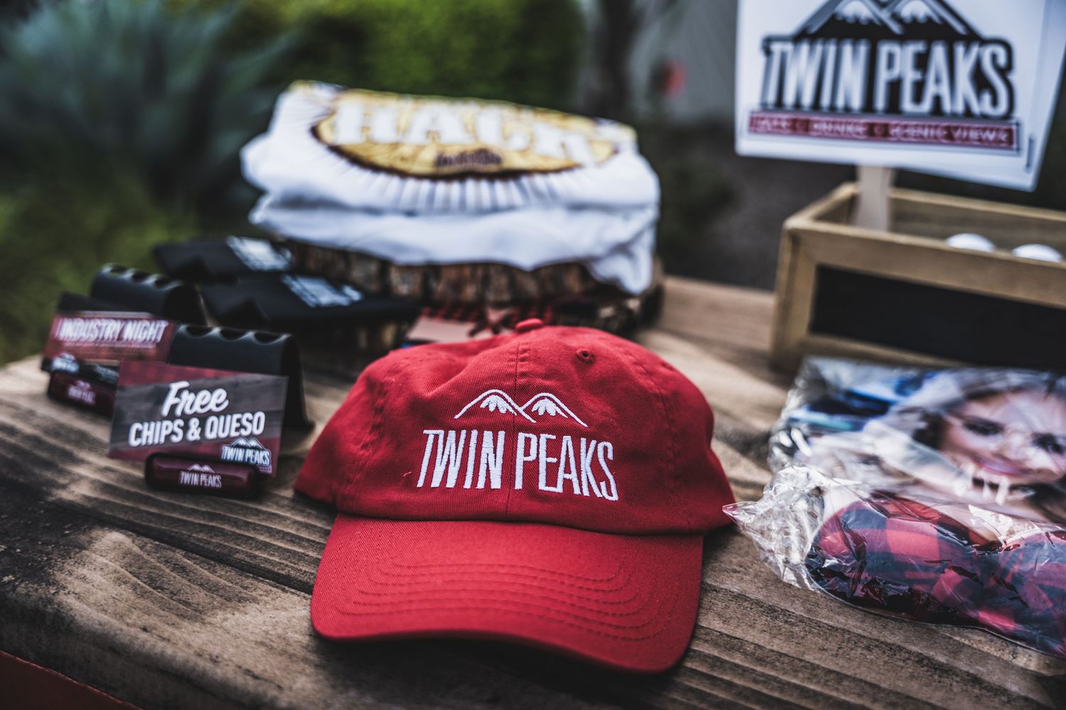 Twin Peaks merchandise display featuring branded baseball caps in red and black on wooden surface.