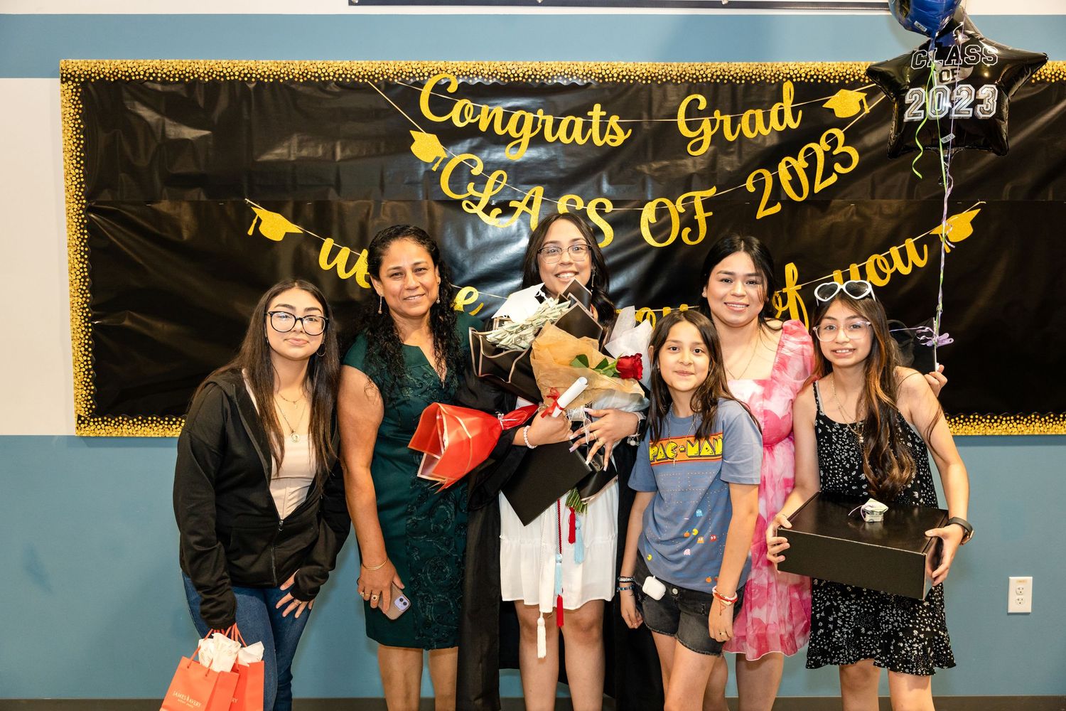 Group poses together in front of congratulatory graduation banner with balloons.