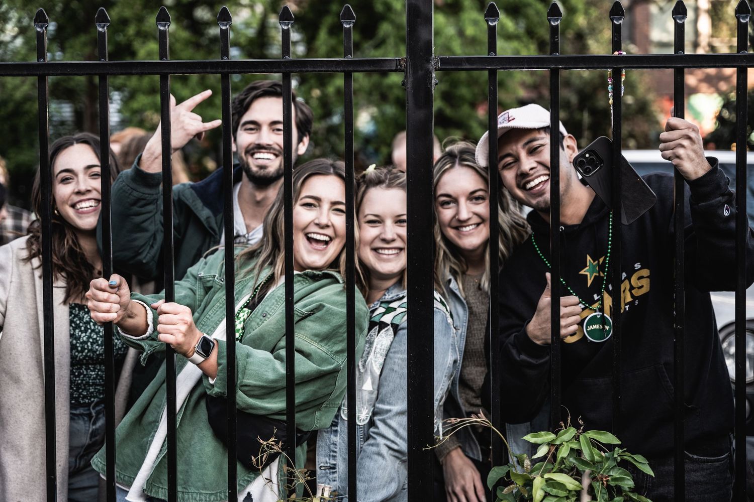 Excited concert crowd poses behind iron fence during outdoor music festival.