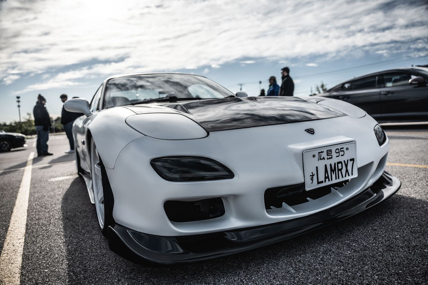 Custom white Mazda RX-7 with aggressive body kit and sports wheels showcased at an outdoor event.