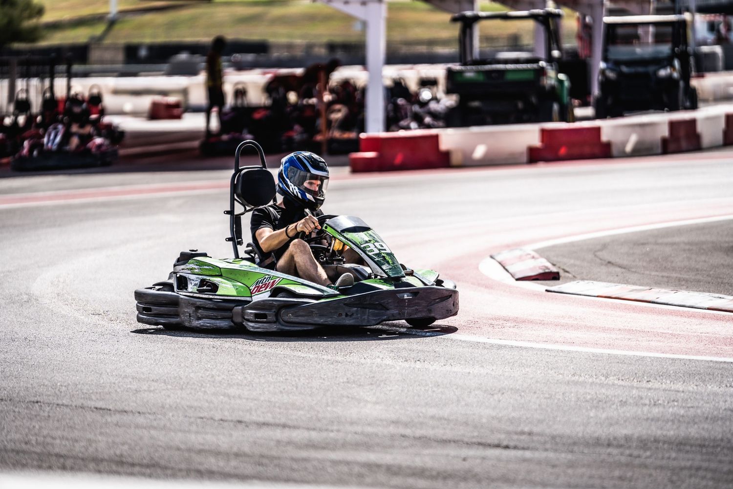 Go-kart racer navigating a turn on an outdoor race track with barriers.