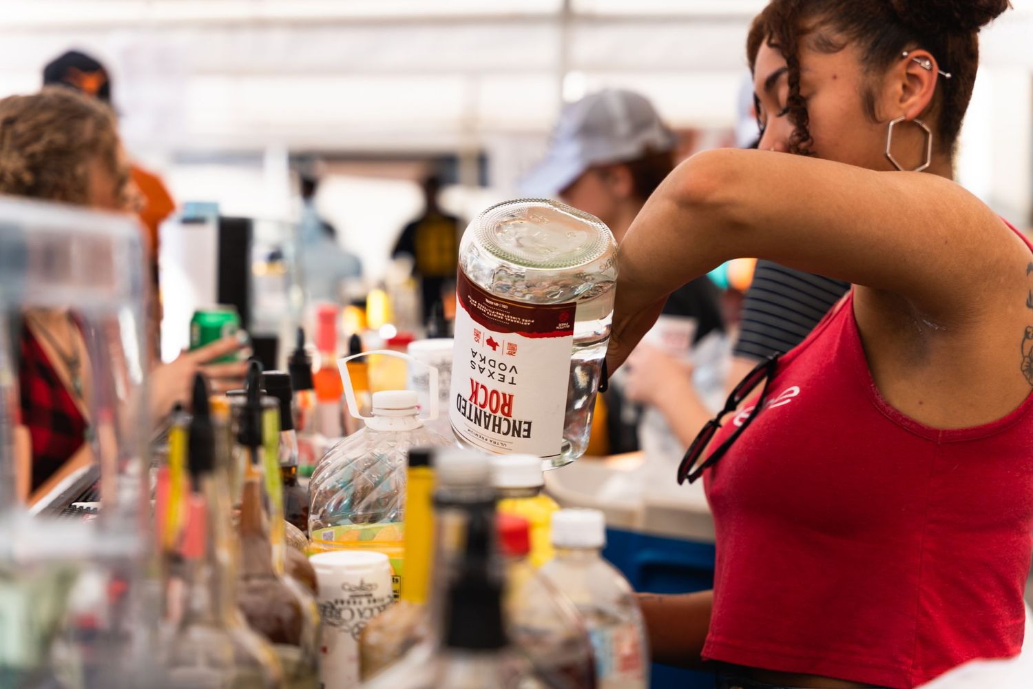 Bartender pouring drinks at outdoor event with bottles and mixers visible.