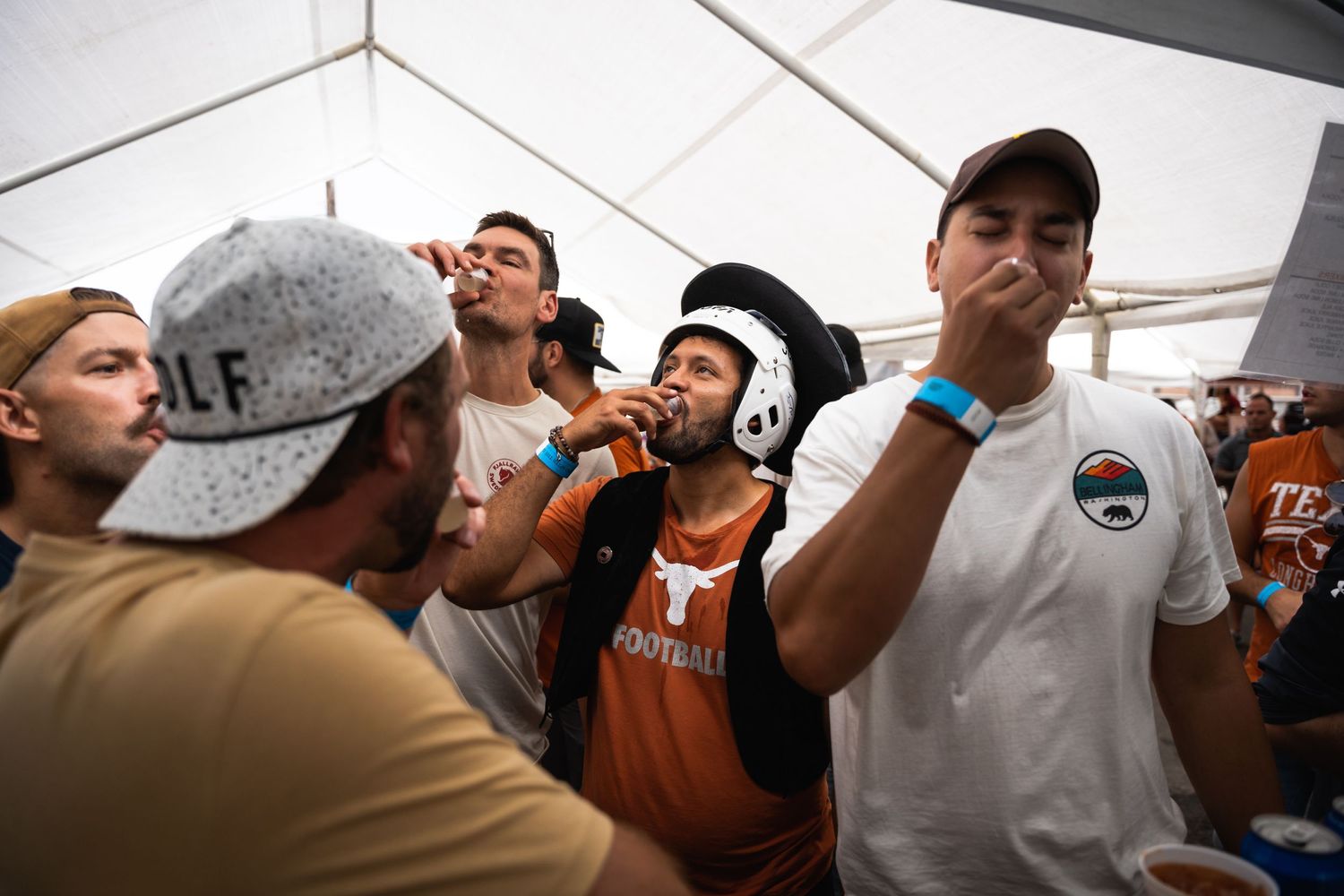Crowd gathered under white tent participating in drinking festivities.
