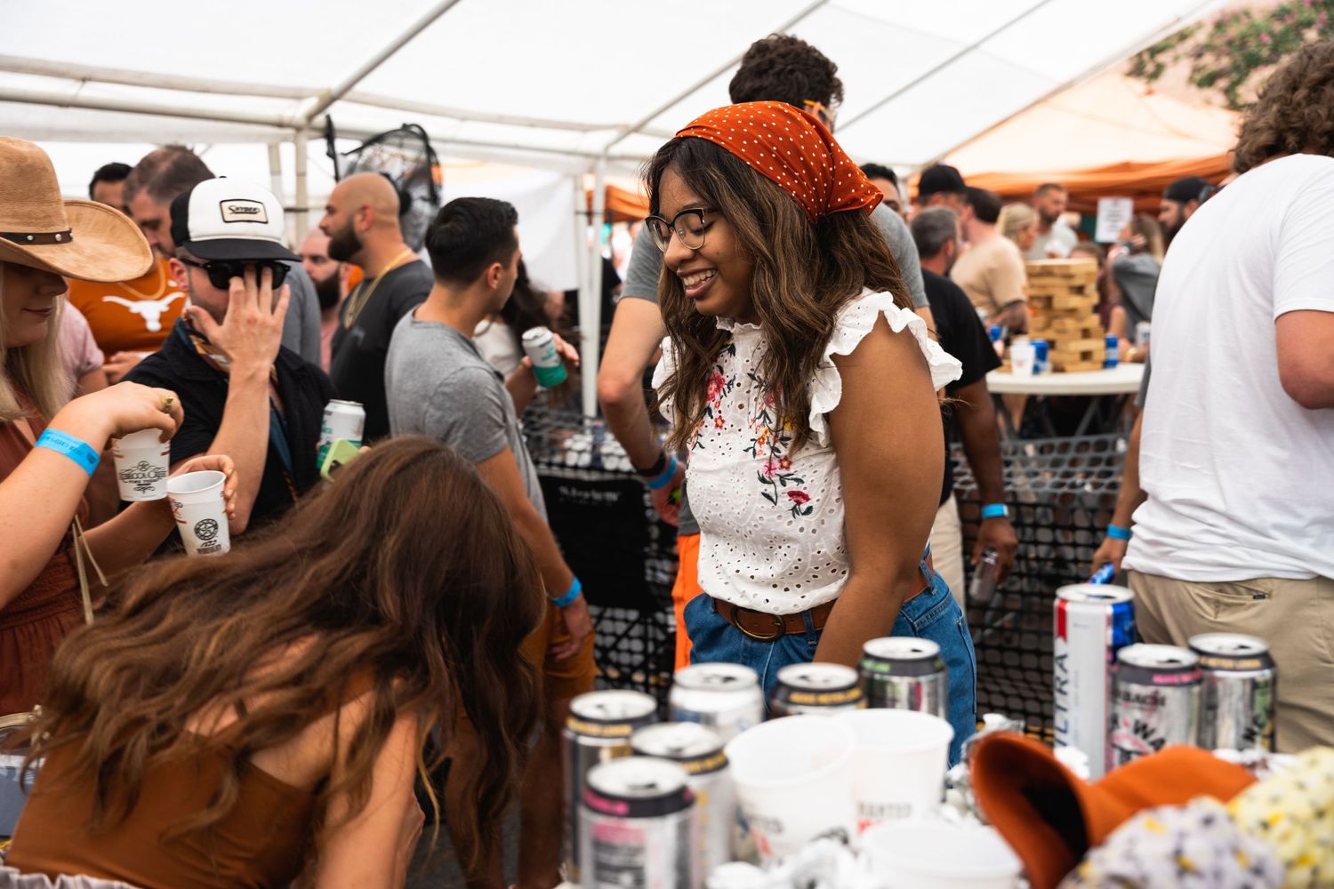 People gathered around a beverage station at an outdoor festival under a white tent.