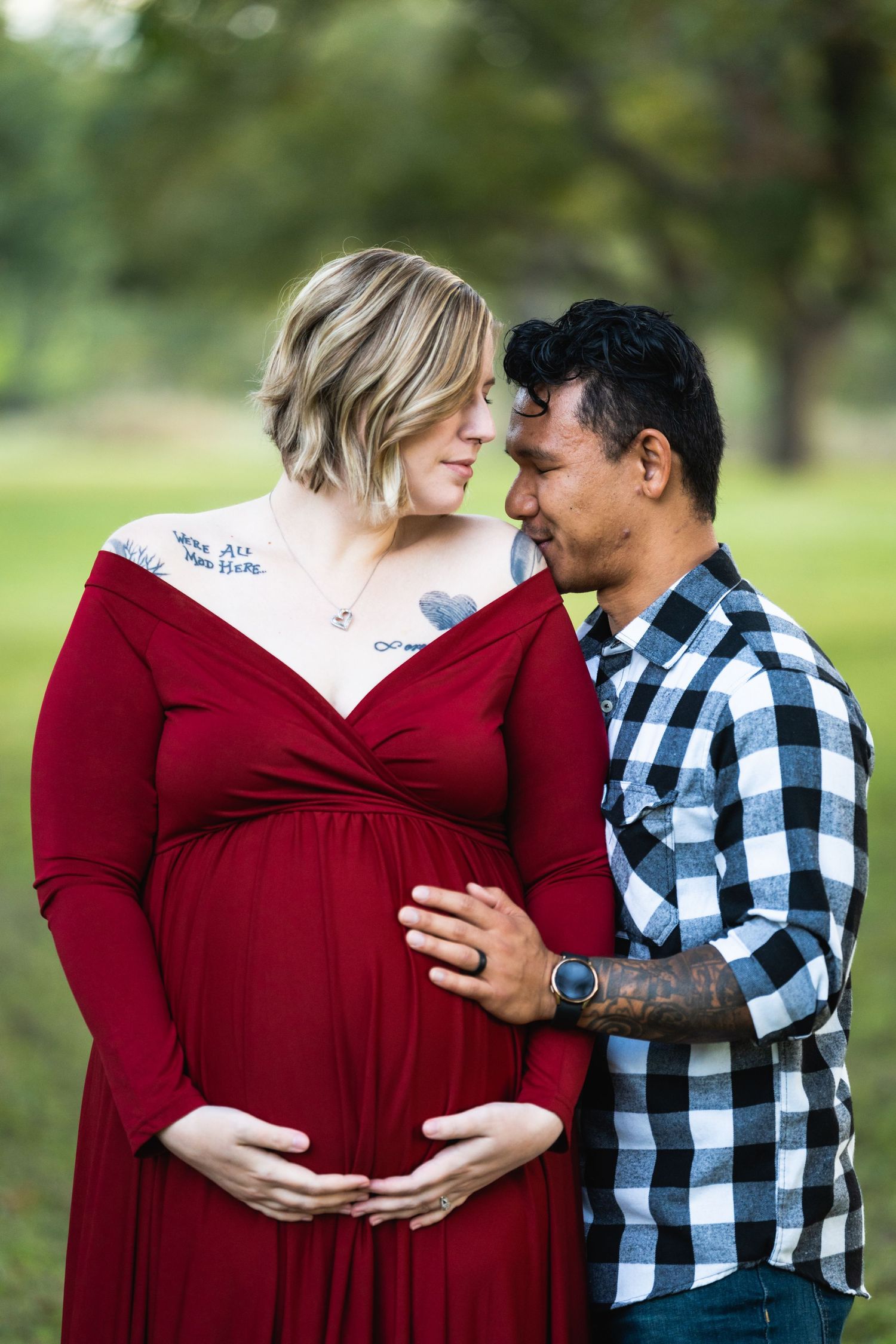 Romantic maternity portrait with couple in red dress and plaid shirt against green background.