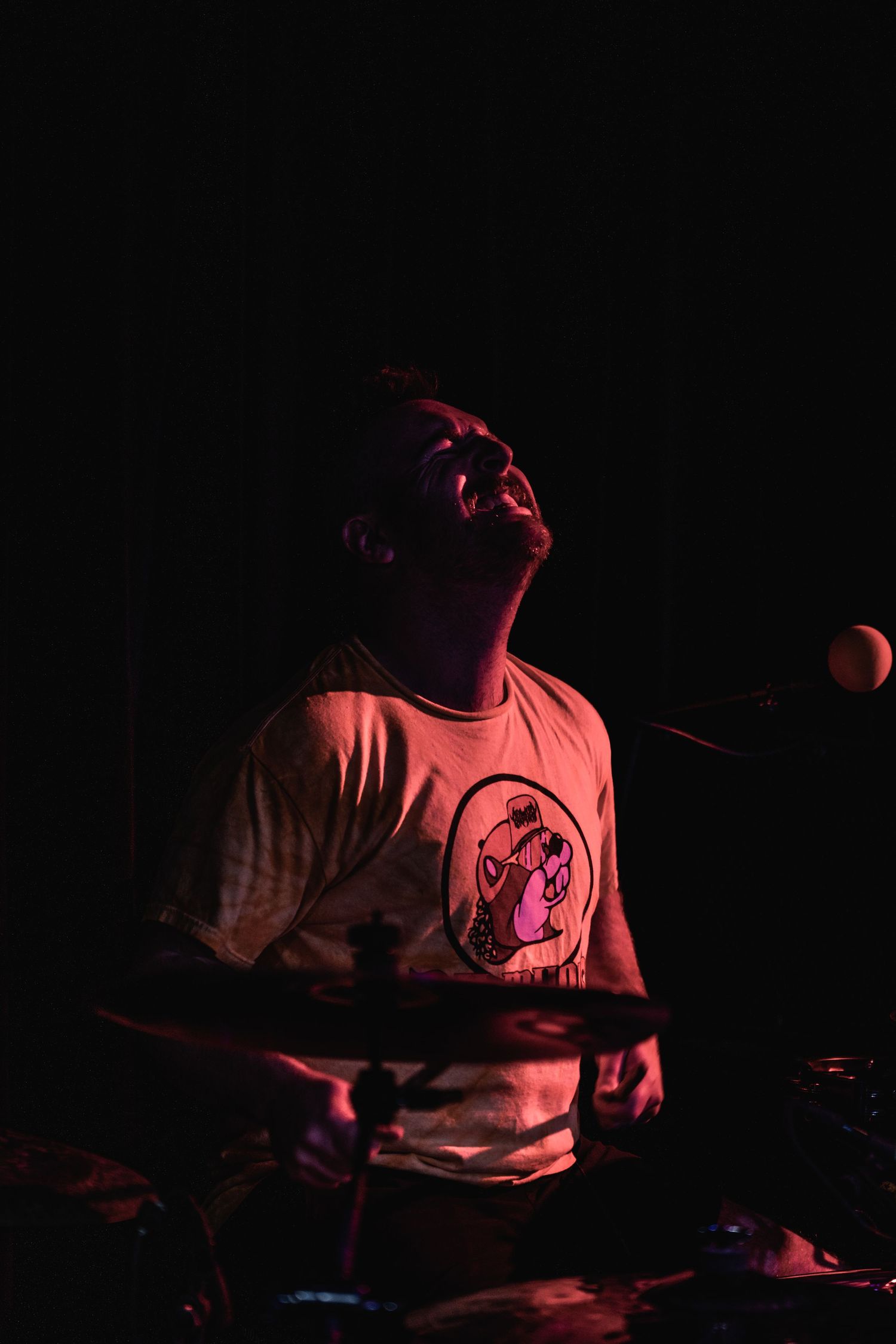 Silhouetted drummer performing passionately under dramatic red stage lighting.