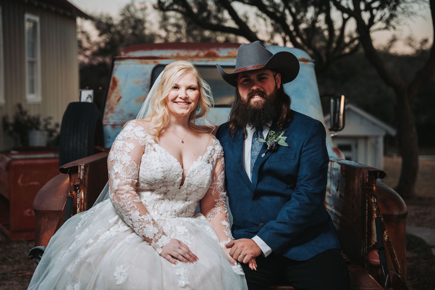 A couple sits in the bed of a vintage red pickup truck at their country-style wedding.