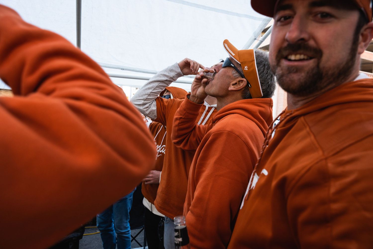 Group of fans in bright orange hoodies gathering at an outdoor sporting event.