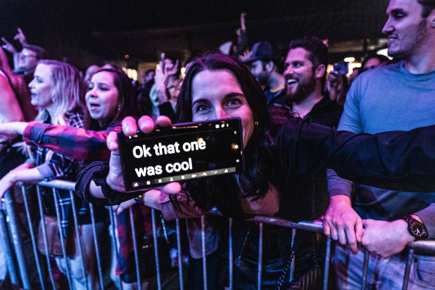 Concert audience behind barriers with illuminated phone screen displaying message.