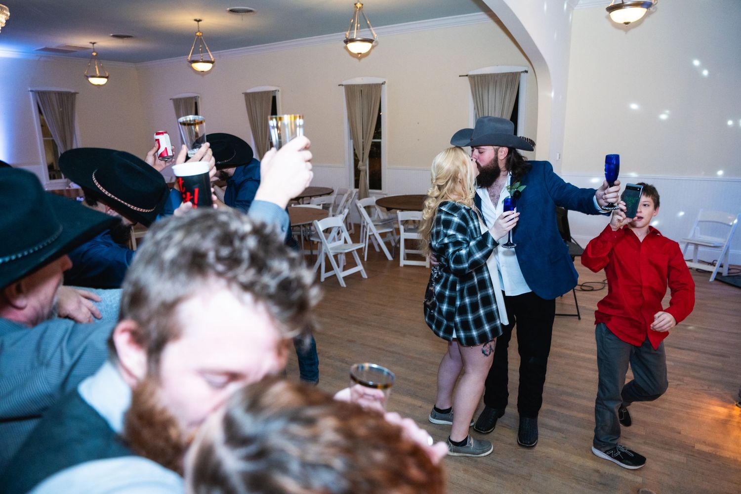 Wedding celebration with guests dancing in casual western attire under ceiling lights.