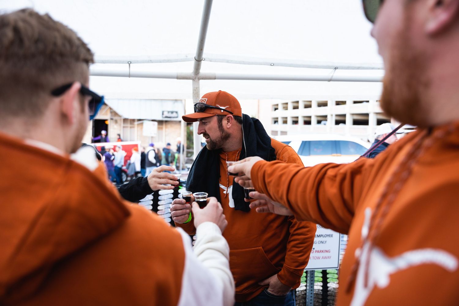 Friends in orange jerseys share drinks at a tailgate party.