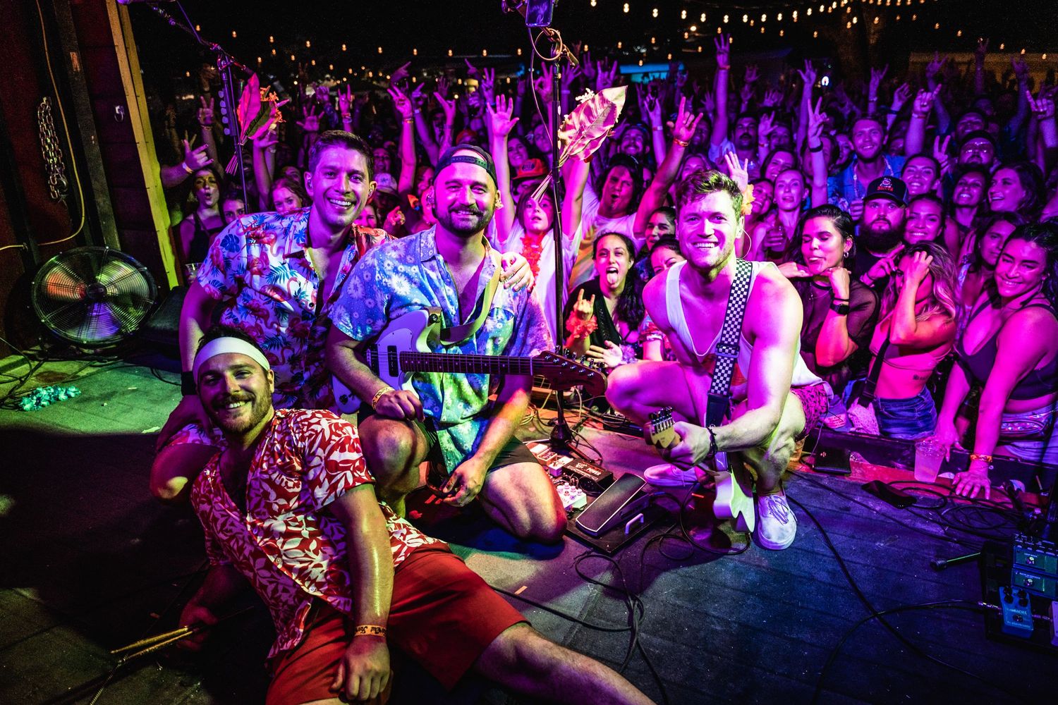 Colorful concert crowd enjoying a lively performance with purple lighting.
