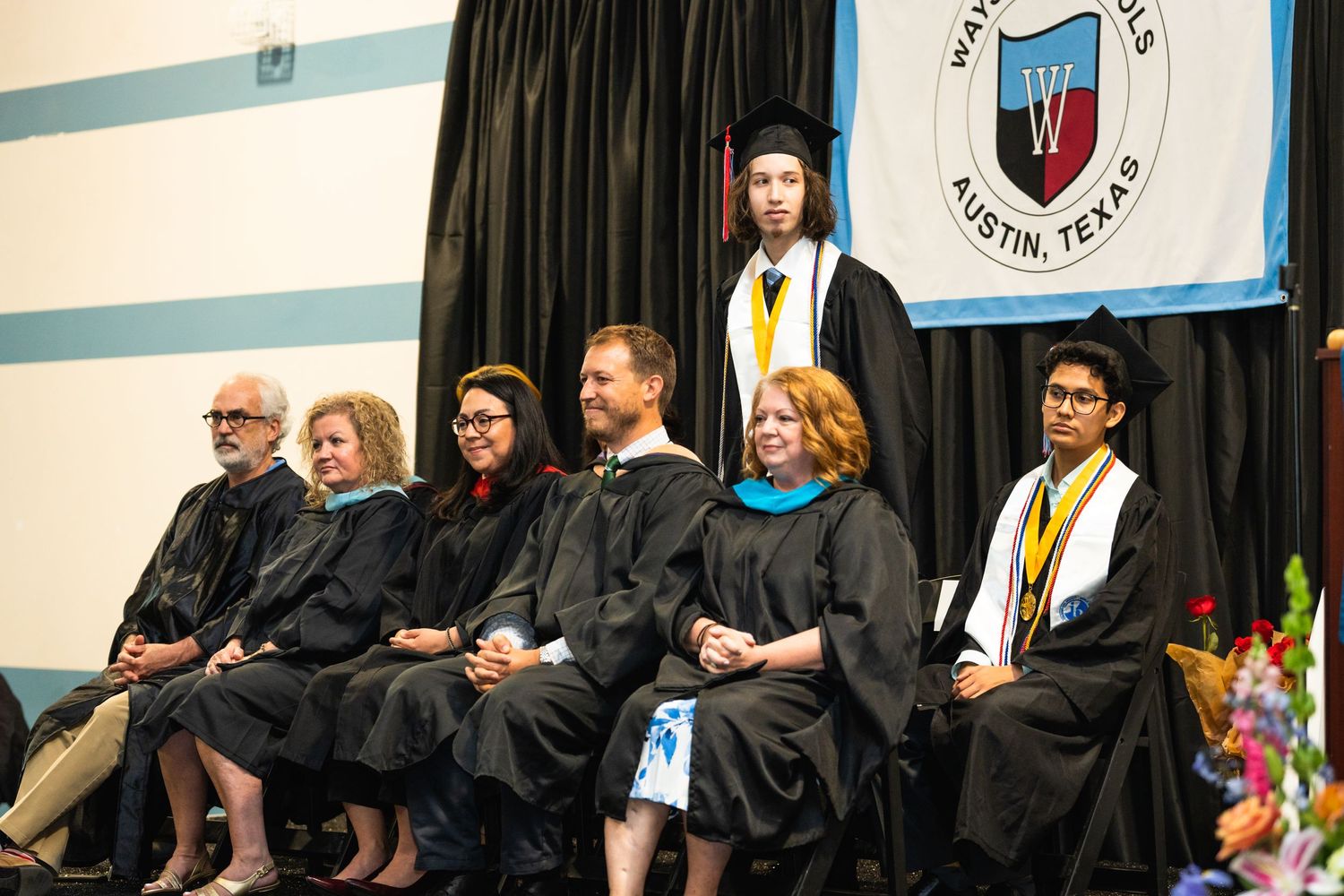 Graduates in black robes and faculty seated during a formal academic ceremony.