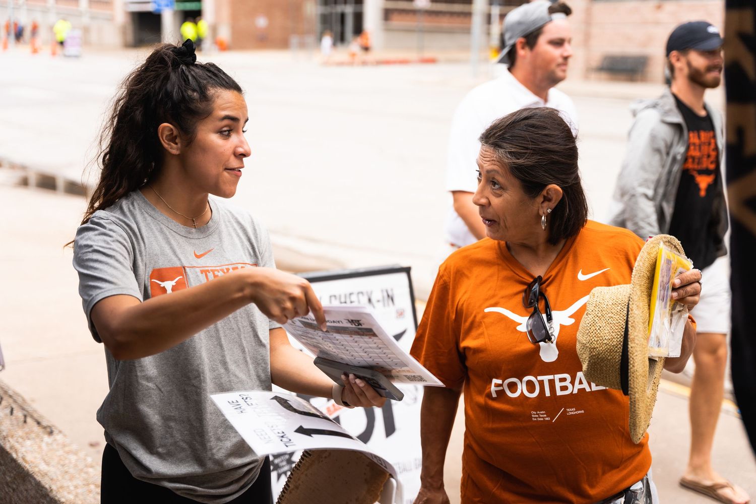 Two people having an animated conversation while wearing orange and grey shirts outdoors.
