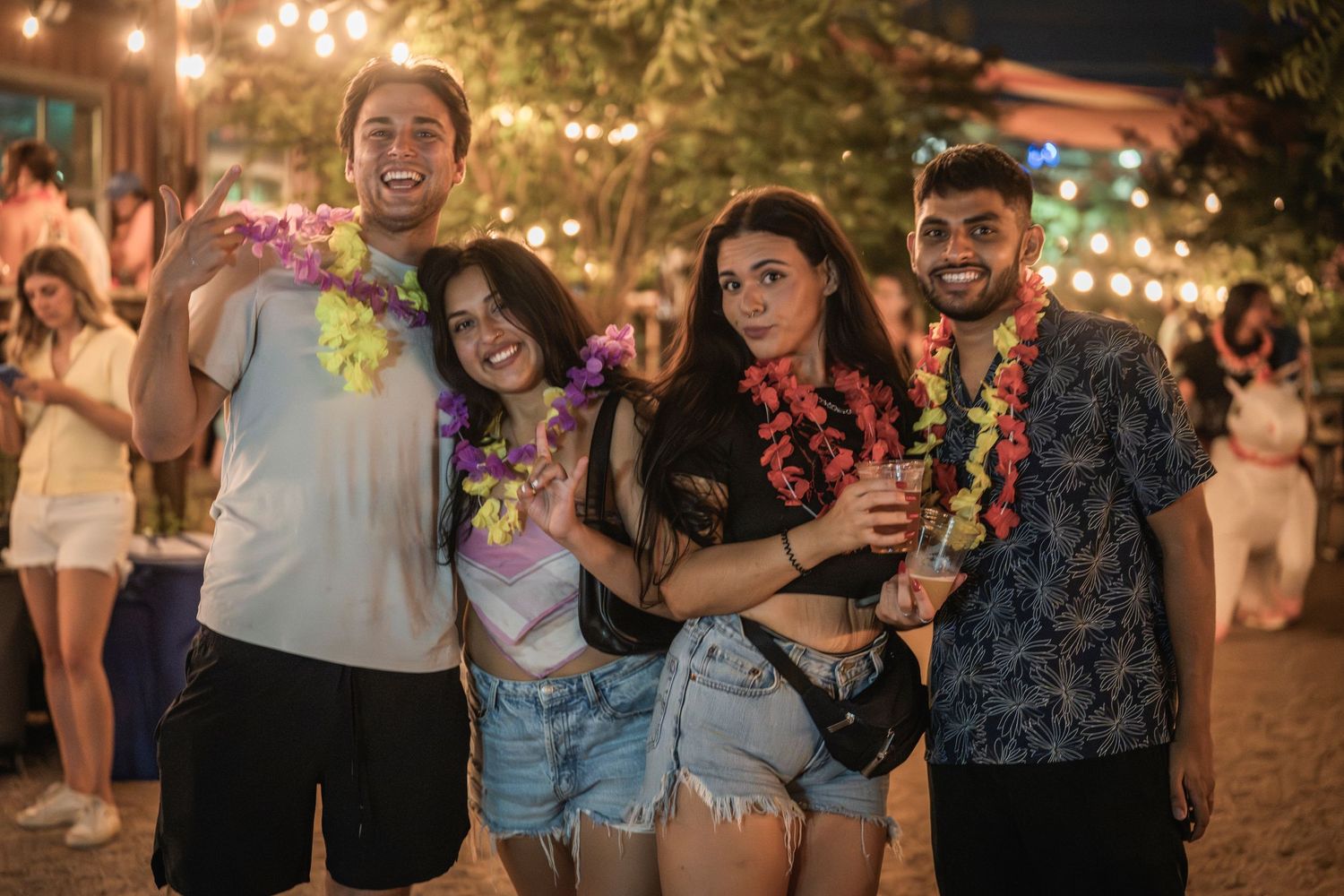 A lively outdoor party scene at night with string lights and people dancing and socializing in a festive atmosphere.