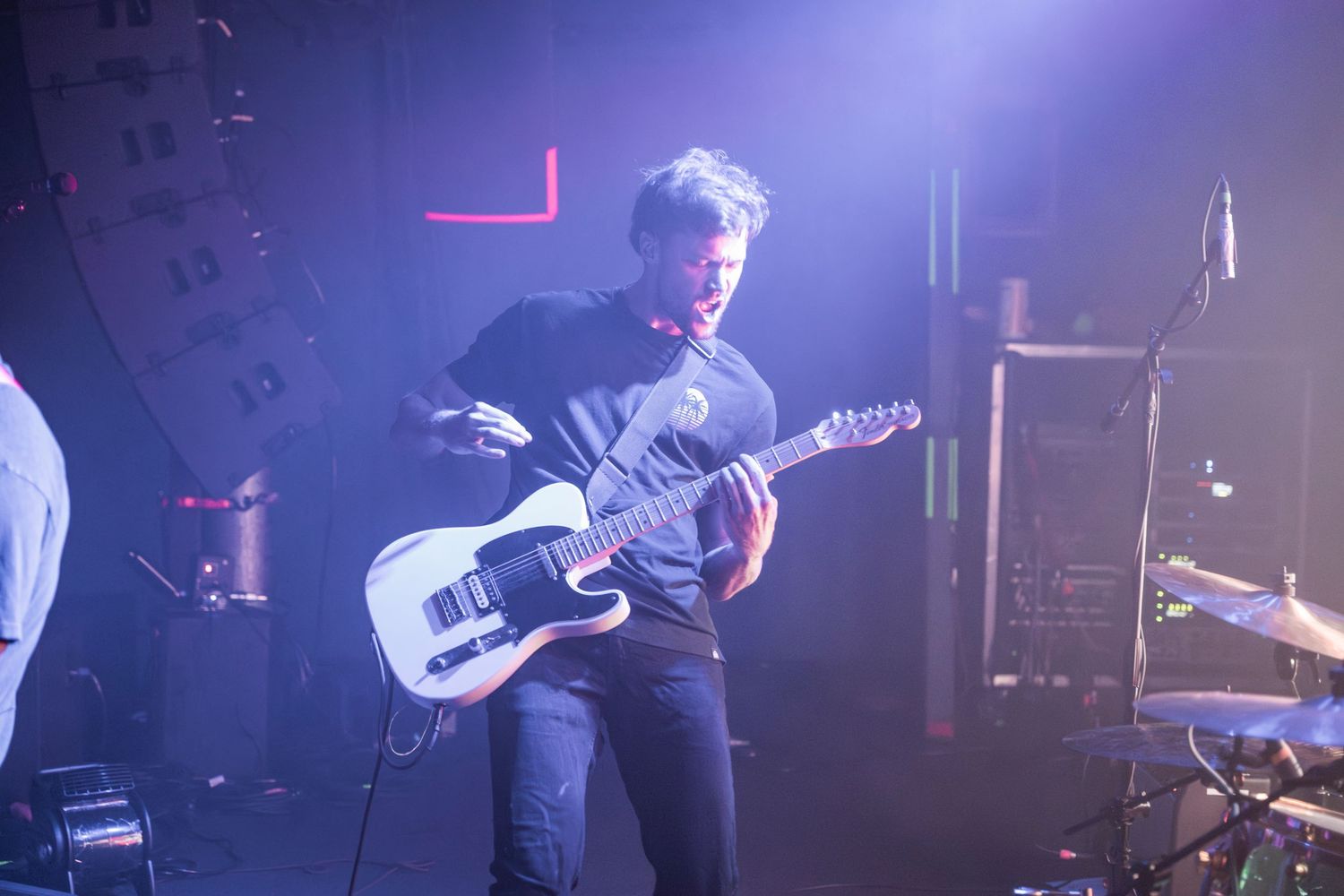 Musicians perform on stage with electric guitars and drums in a dark concert venue with dramatic blue lighting.