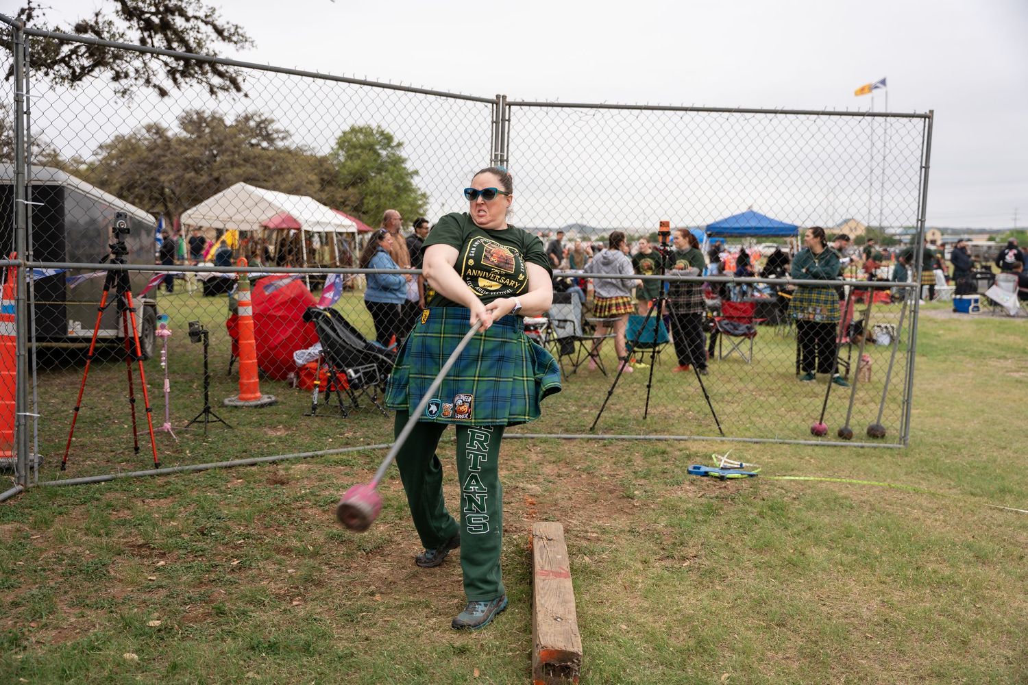 Woman in green tartan kilt competing in Highland Games hammer throw at outdoor festival.