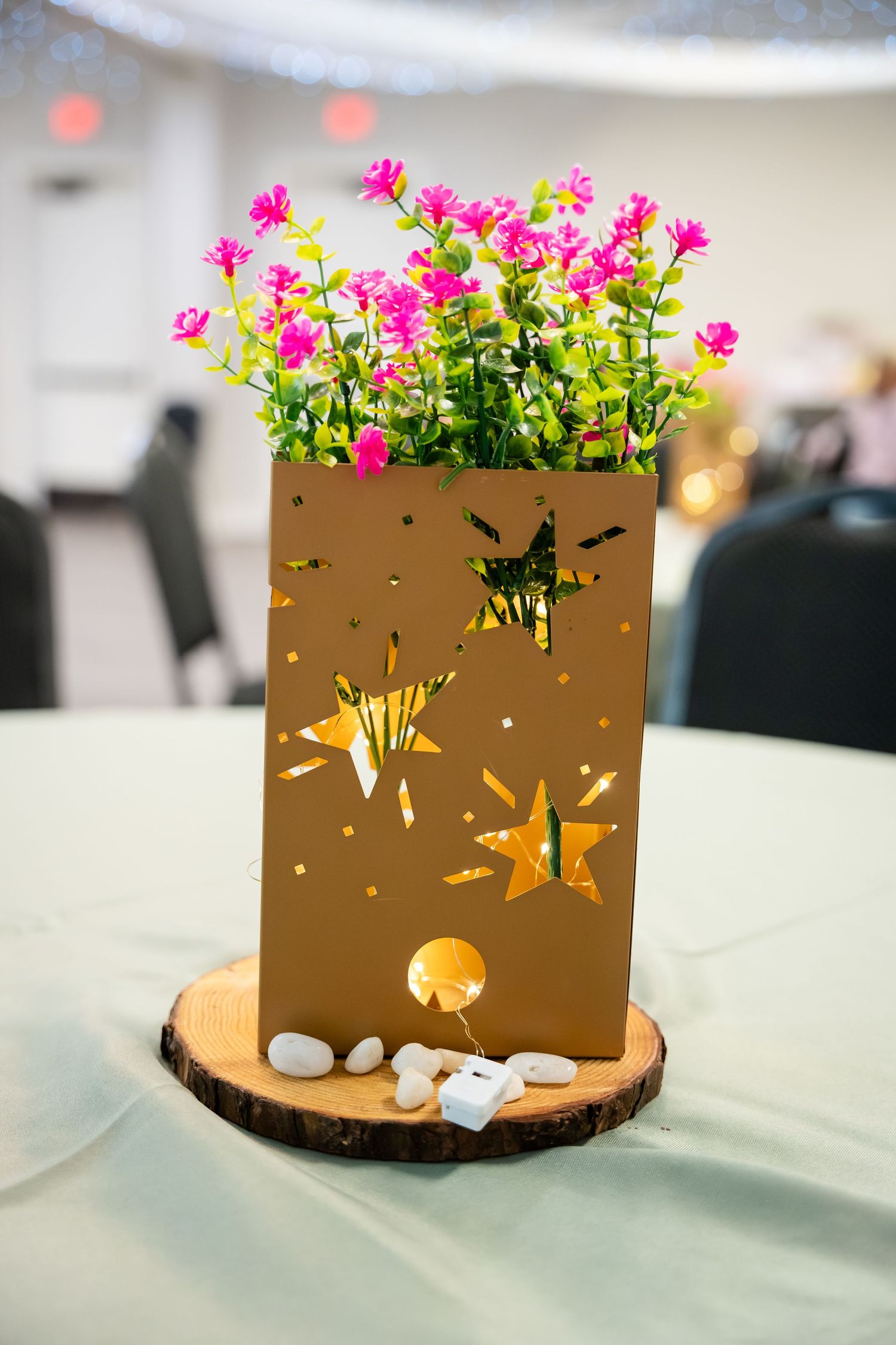 Gold star-cutout vase with pink wildflowers on wood slice centerpiece, decorated with white stones on a mint green tablecloth.