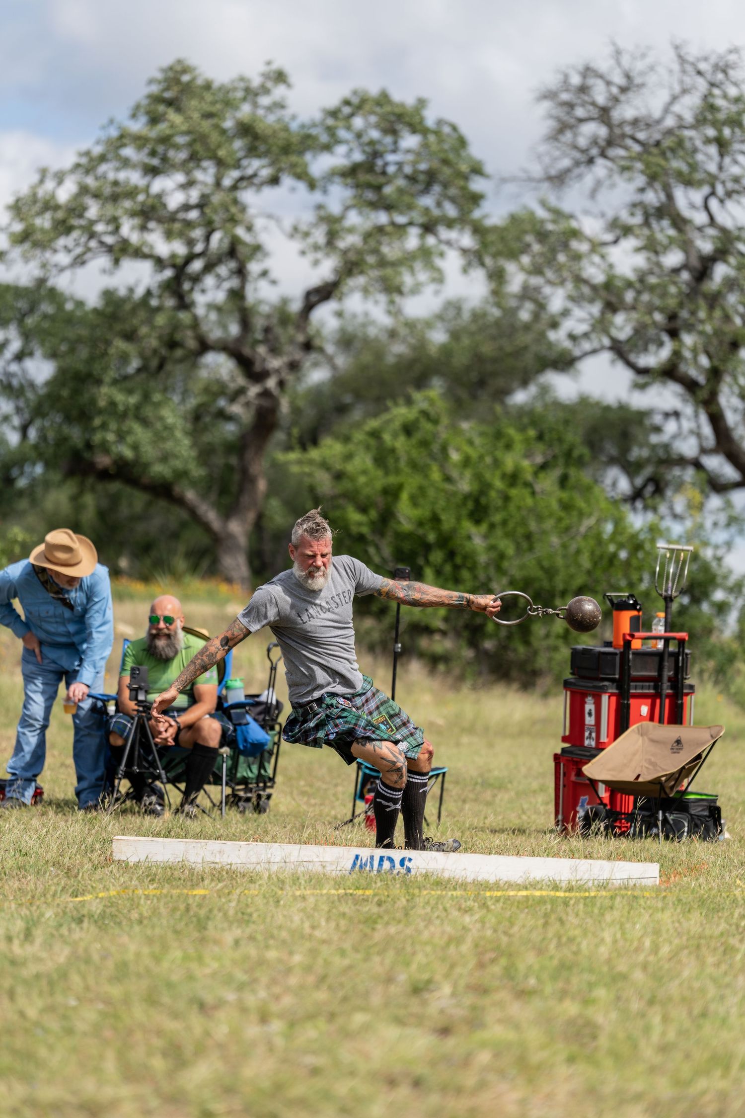 Man in kilt throws heavy weight at Scottish Highland Games competition outdoors.