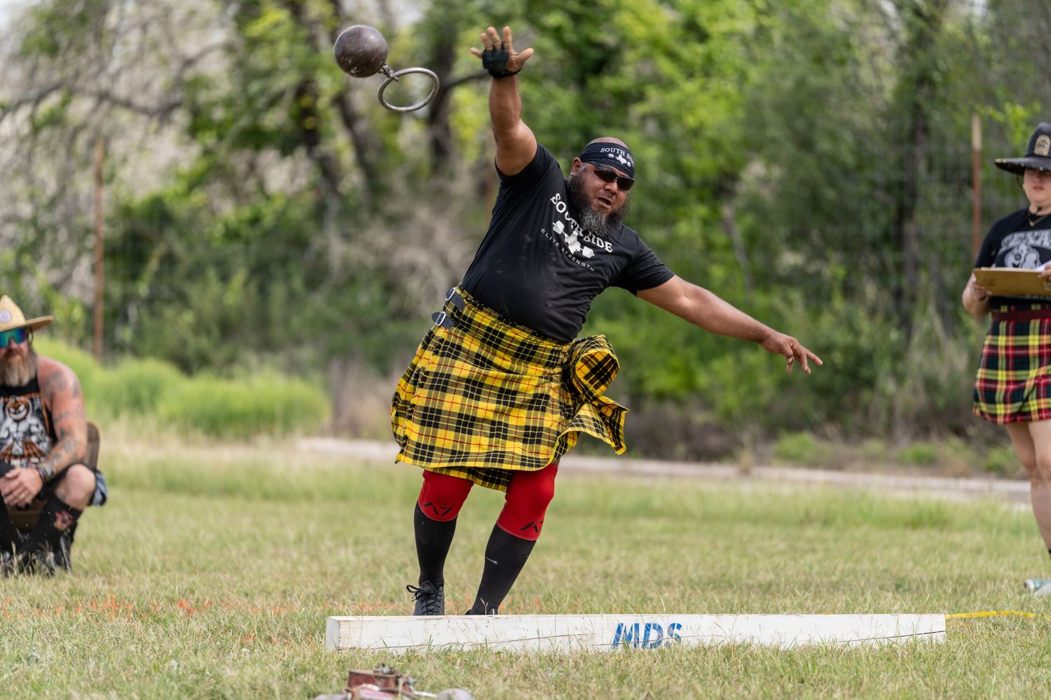 Athlete in tartan kilt competes in Highland Games hammer throw event outdoors.