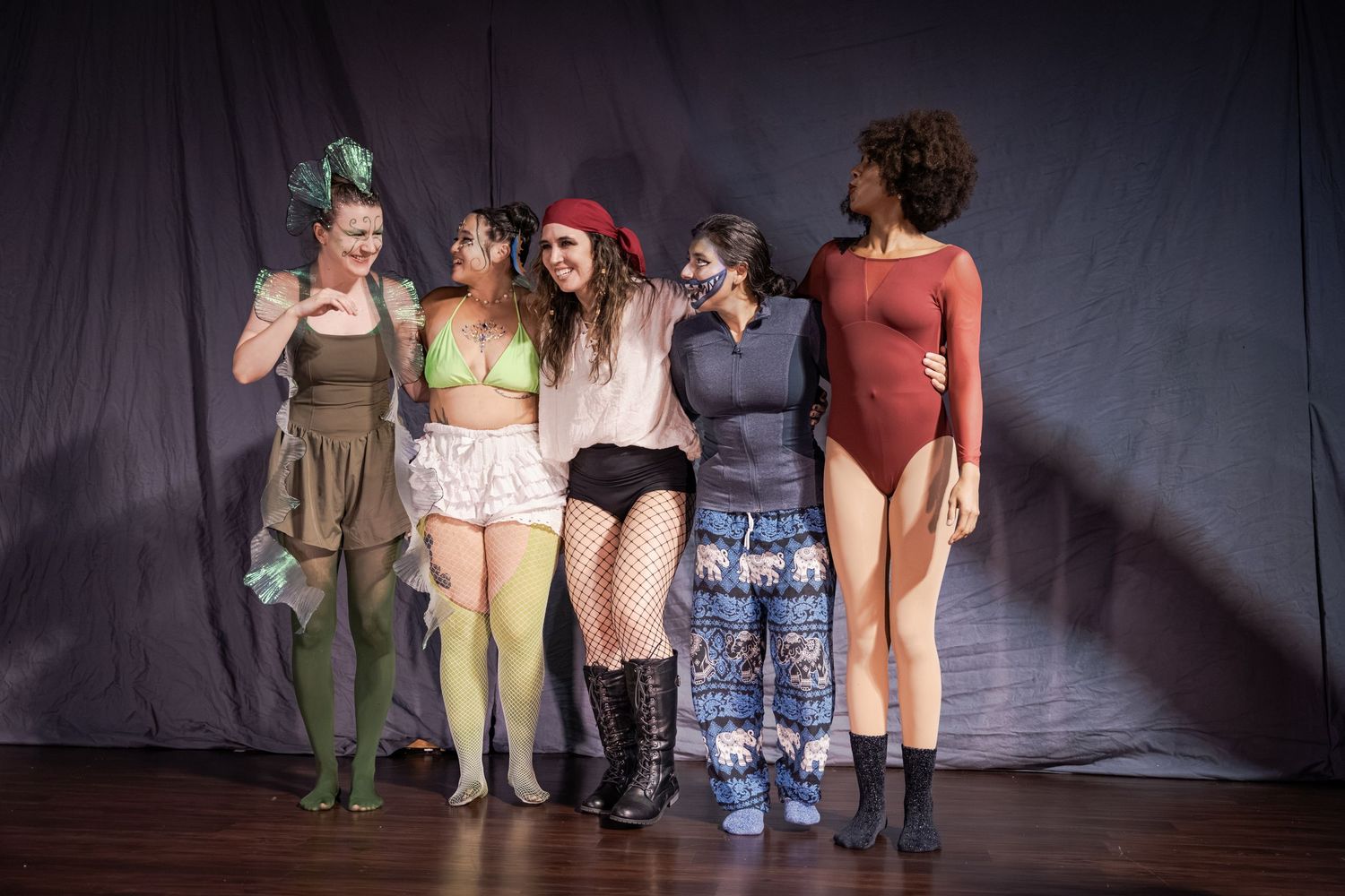 Five women in colorful costumes pose together on a stage during a theatrical performance.