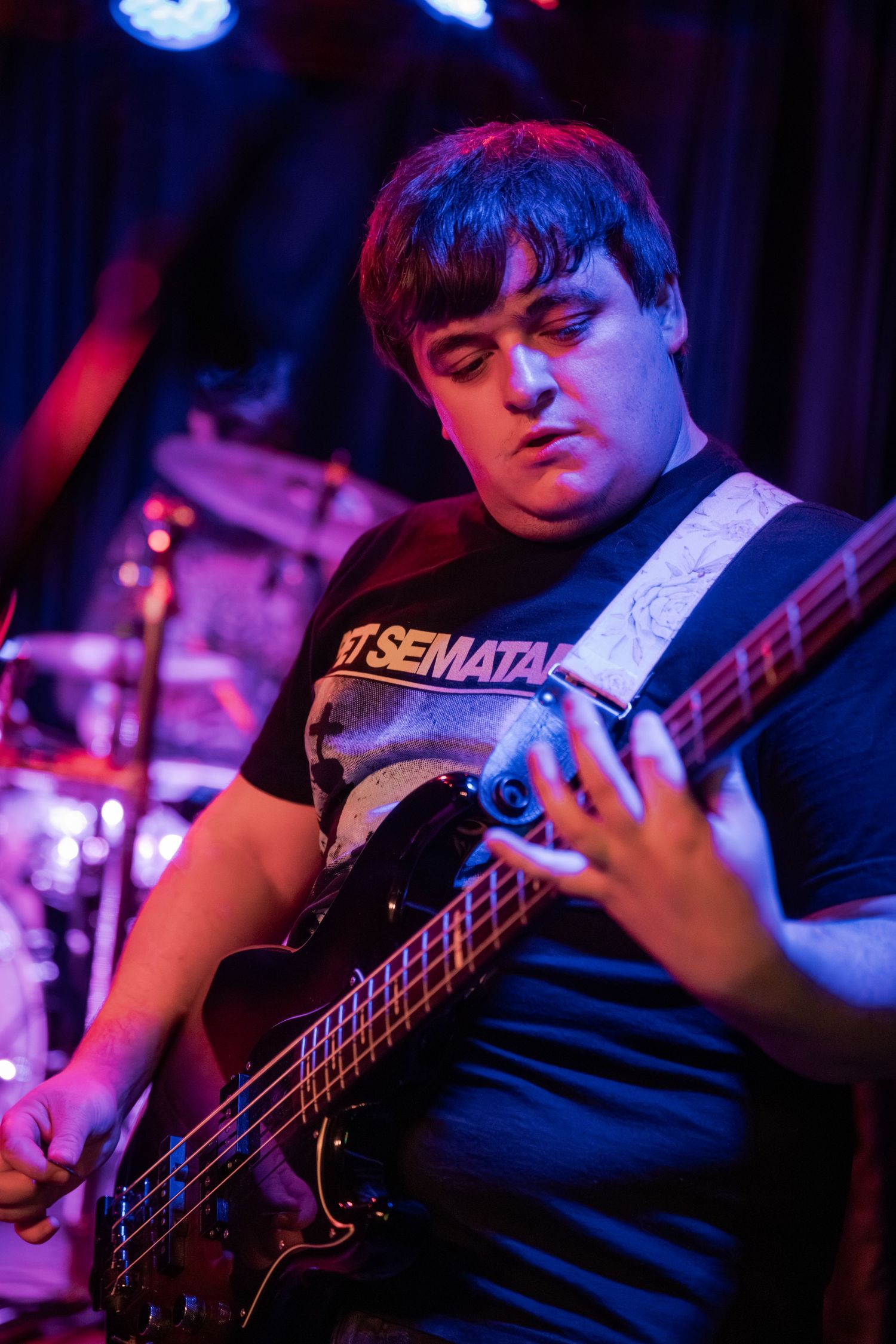 Bass guitarist performing on stage in dark lighting with blue and purple spotlights creating moody atmosphere.