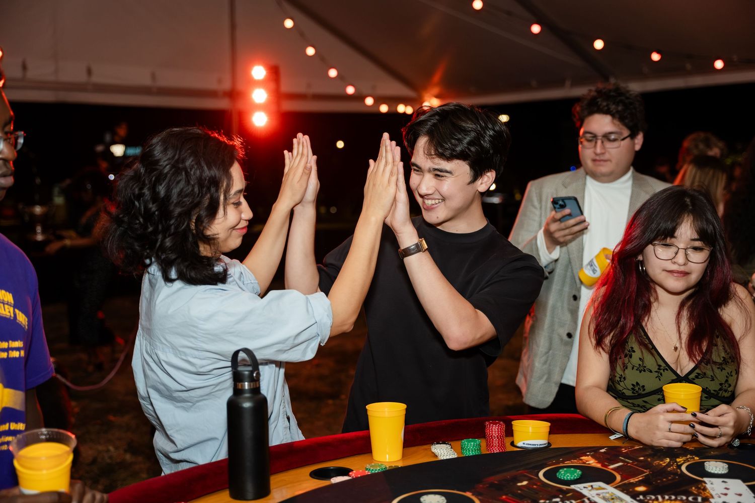 People dancing and socializing at a dimly lit nightclub or party venue with colorful lighting and drinks.