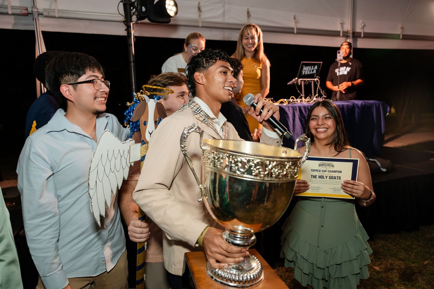 A group celebrates with a large trophy at an event while dressed in casual and formal attire.