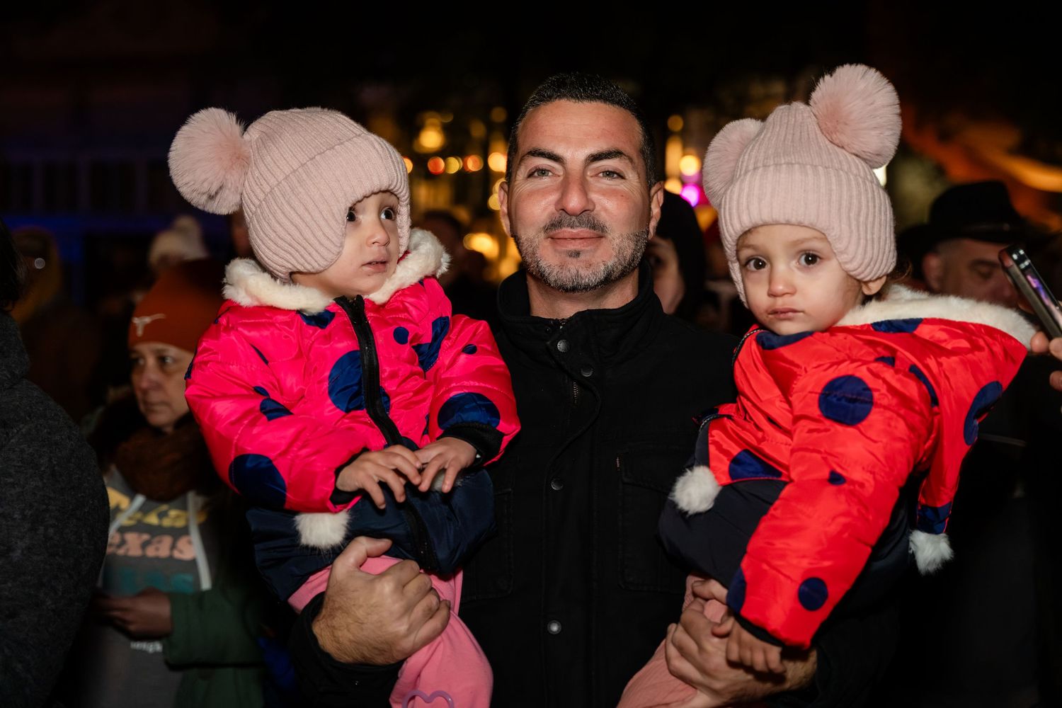 A series of candid nighttime photos showing adults holding a small child wearing a bright red winter coat.
