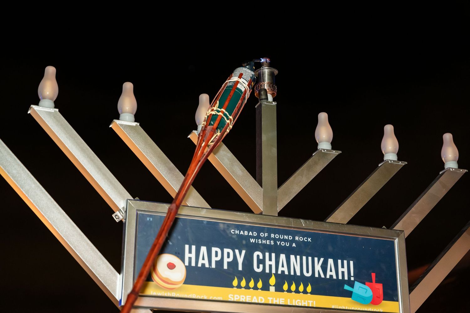 Illuminated Hanukkah menorah display glows brightly against dark sky during holiday celebration.