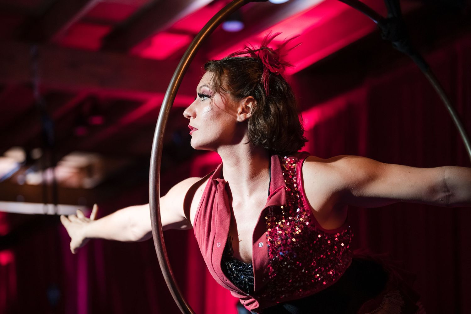 A performer in a red sequined outfit sings passionately on stage under dramatic pink lighting.