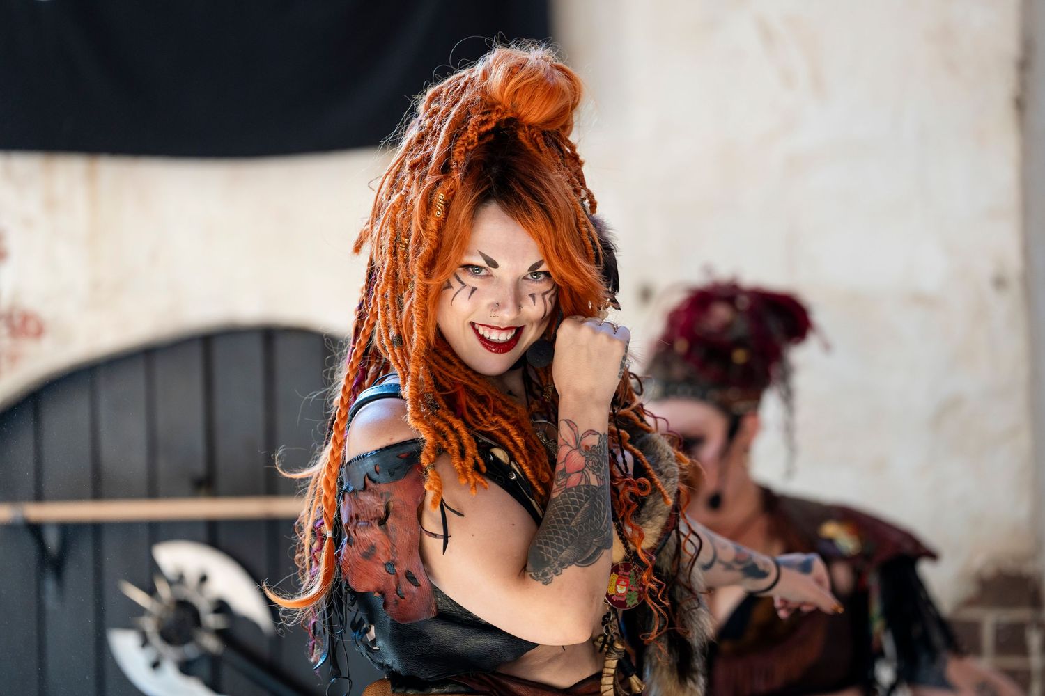A person with vibrant red hair smiles while posing against an urban background with blurred elements.
