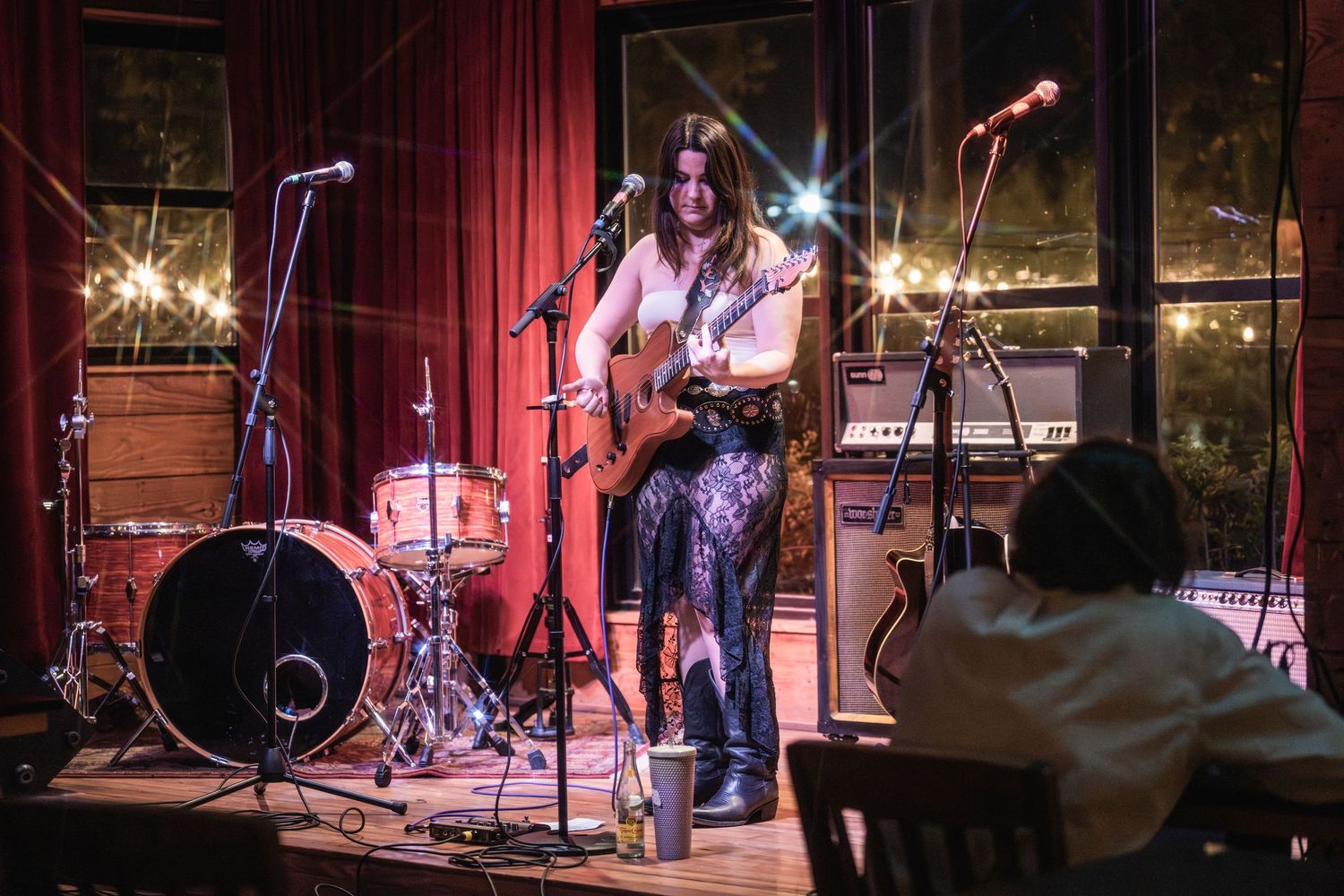 Musicians perform on a dimly lit stage with red lighting and musical equipment visible in the background.