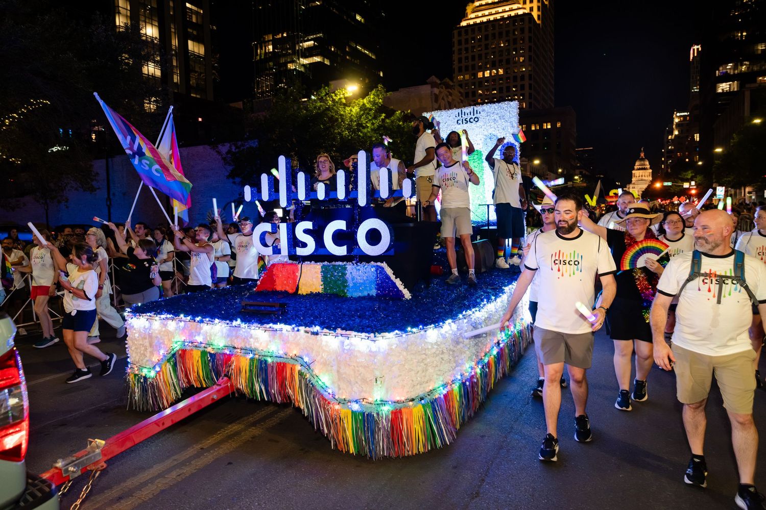 Cisco Pride parade float with rainbow lights and decorations, surrounded by celebrating participants at night.