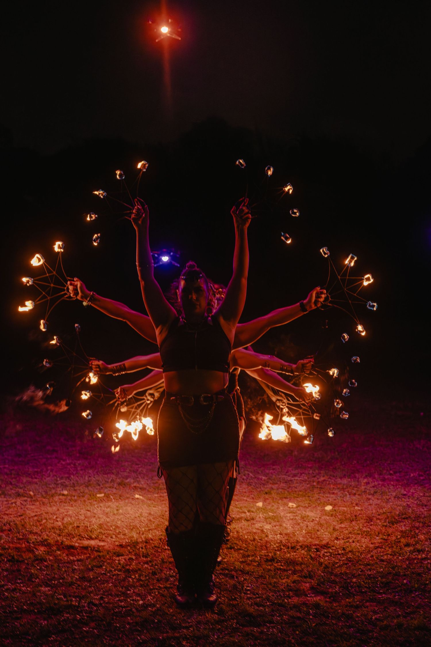 Fire dancer performing at night with glowing spinning poi creating dramatic light trails against dark sky.