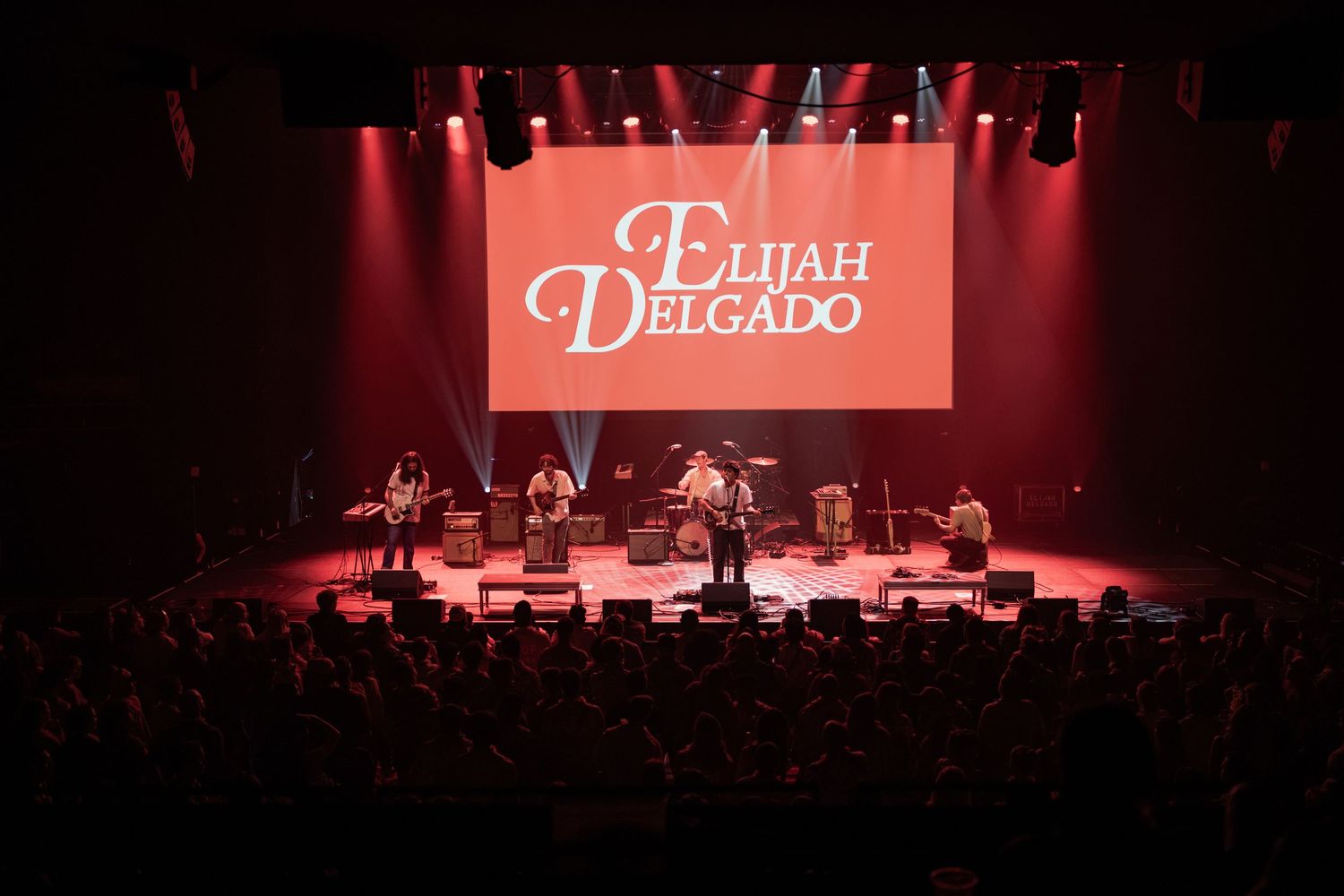 Elijah Delgado performing live on stage with full band under red lights before a large crowd.