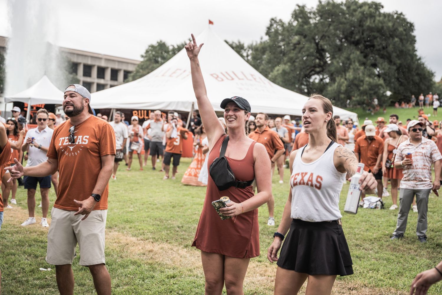 Crowd of people in burnt orange and white attire celebrating at an outdoor festival with white tents in background.