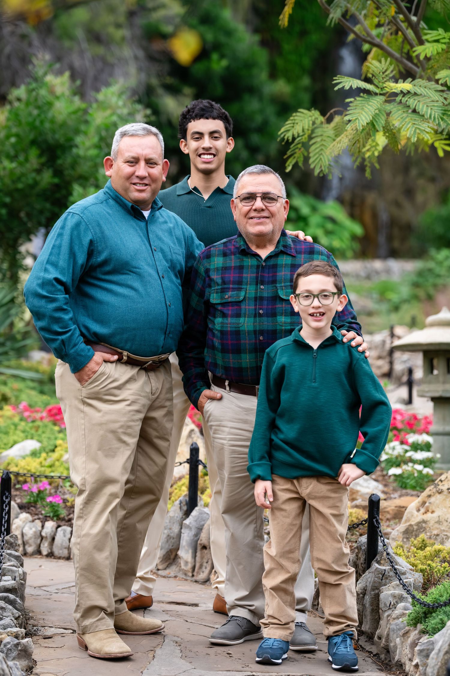 Three generations pose together in matching outfits among a garden setting with flowers and greenery.