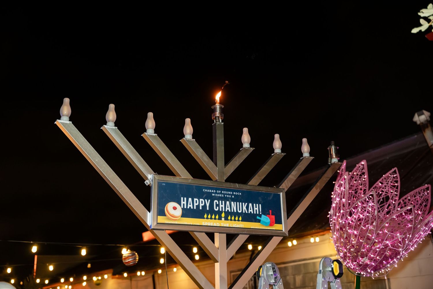 A series of outdoor Hanukkah menorah displays illuminated at night with glowing candles and decorative lights.