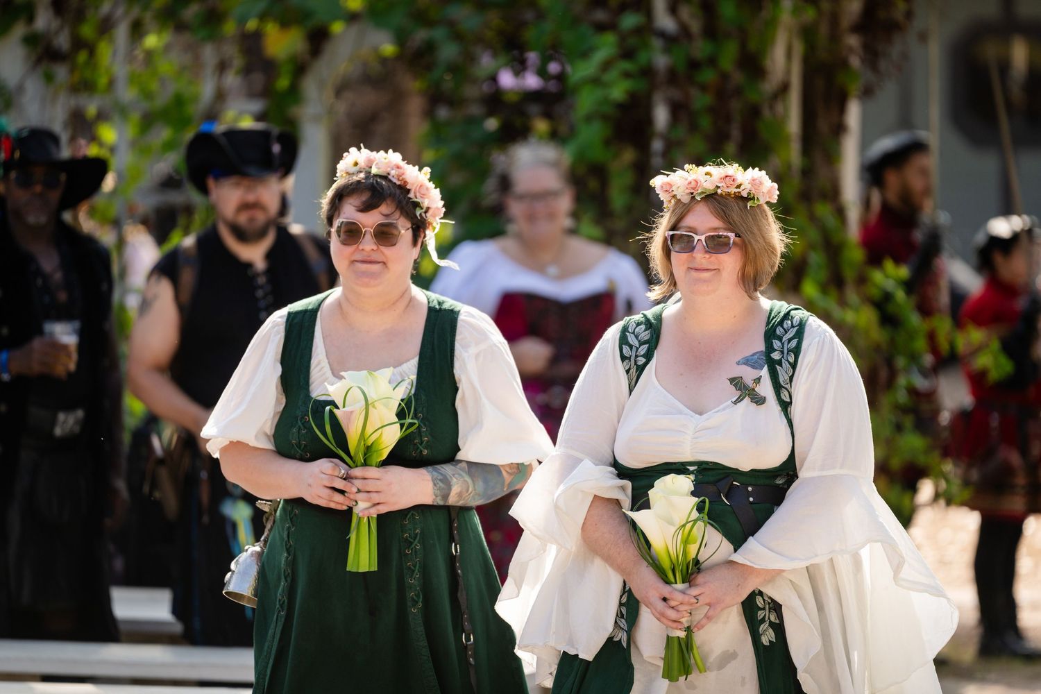 A wedding party walks through a garden setting with bridesmaids in green dresses and white floral bouquets.
