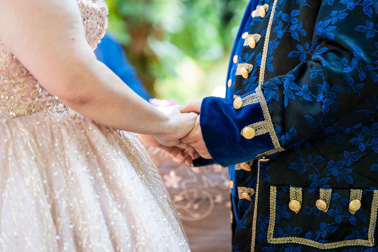 A couple in formal wedding attire holds hands during an outdoor ceremony with blue and gold decor.