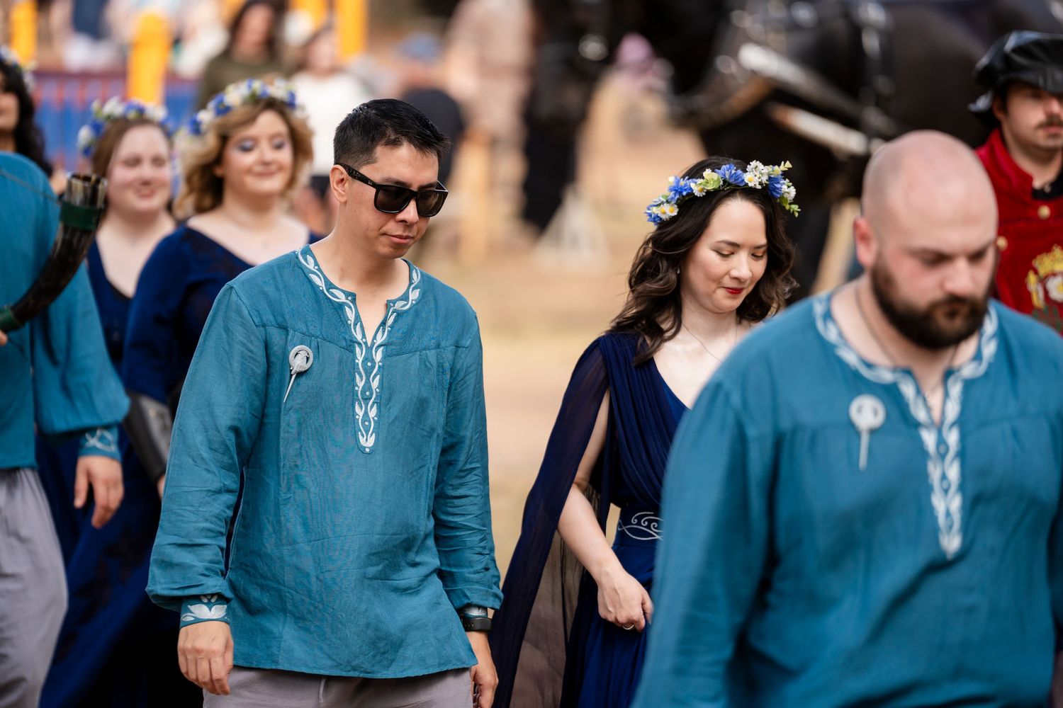 A group of people wearing blue medieval renaissance costumes walking together at an outdoor festival.