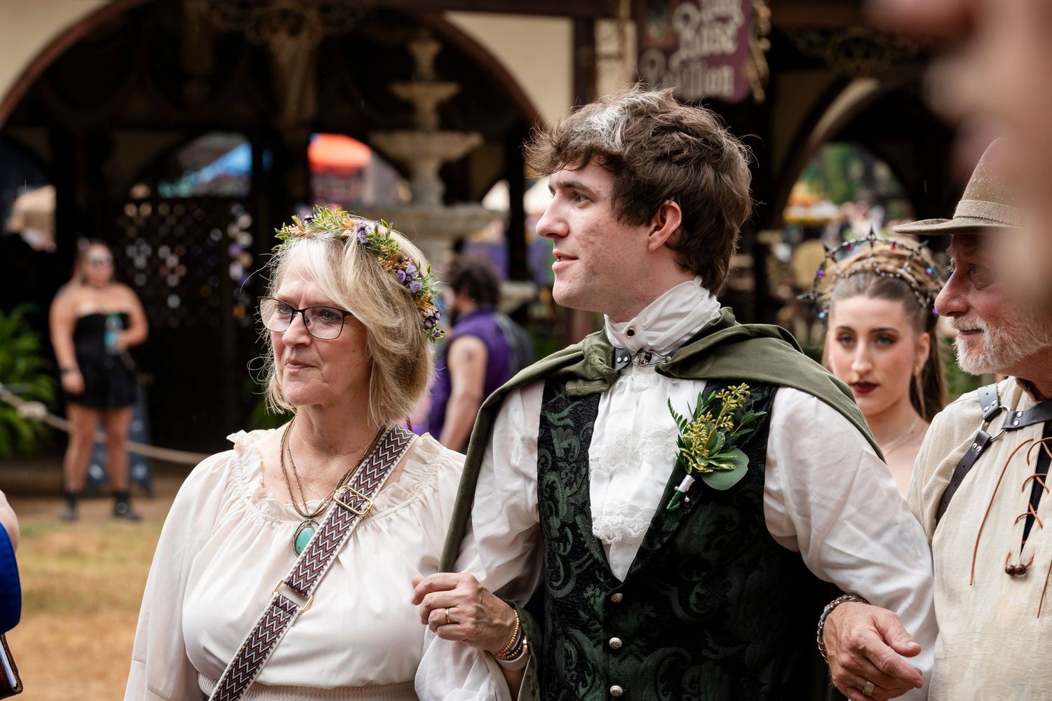 A group of people in medieval renaissance fair costumes with floral accessories and period clothing at an outdoor event.