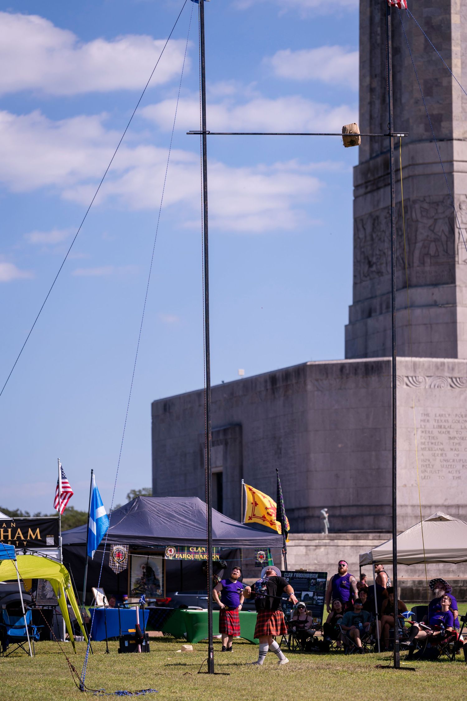 Colorful tents and flags set up near large concrete pillars under a blue sky with white clouds.