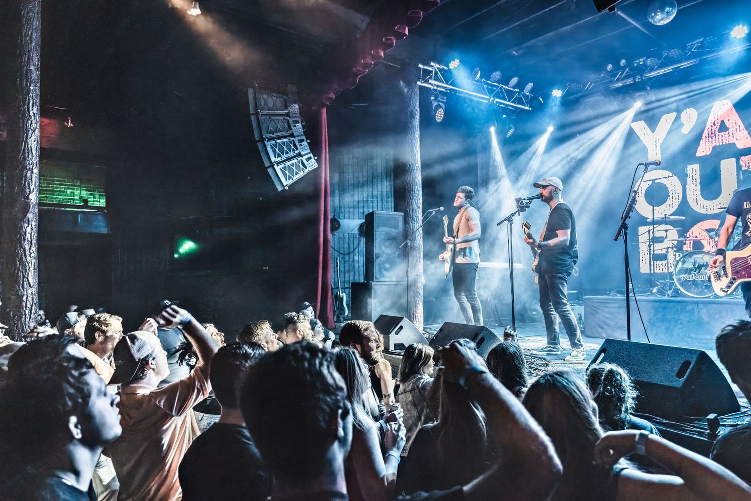 Concert crowd watching performers on stage with blue lighting and smoke effects.