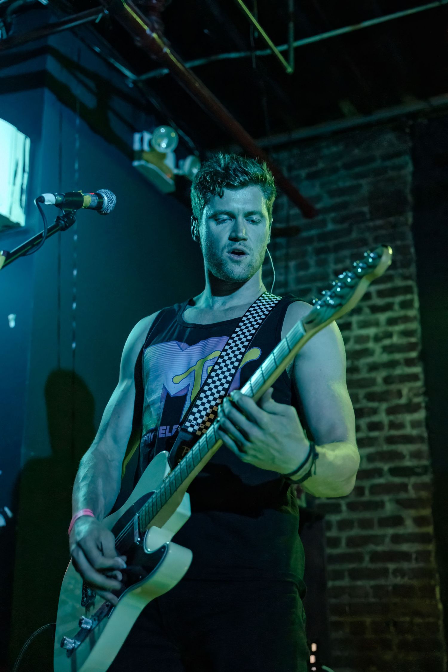 Bassist performing on stage with dramatic blue lighting against brick wall backdrop.