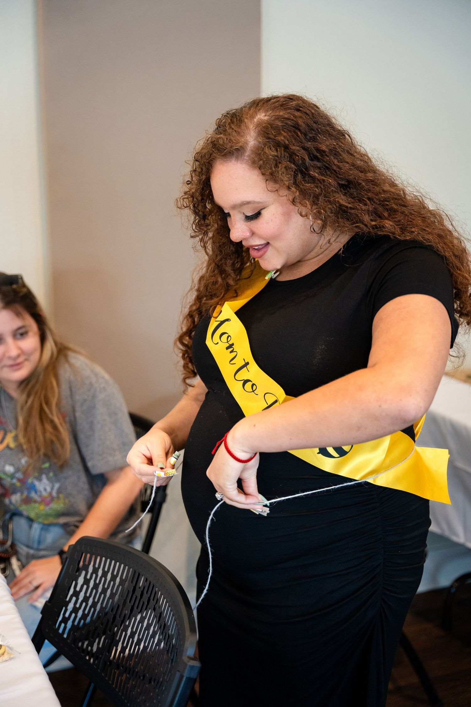 A person wearing a black shirt and yellow sash smiles while participating in baby shower activities.