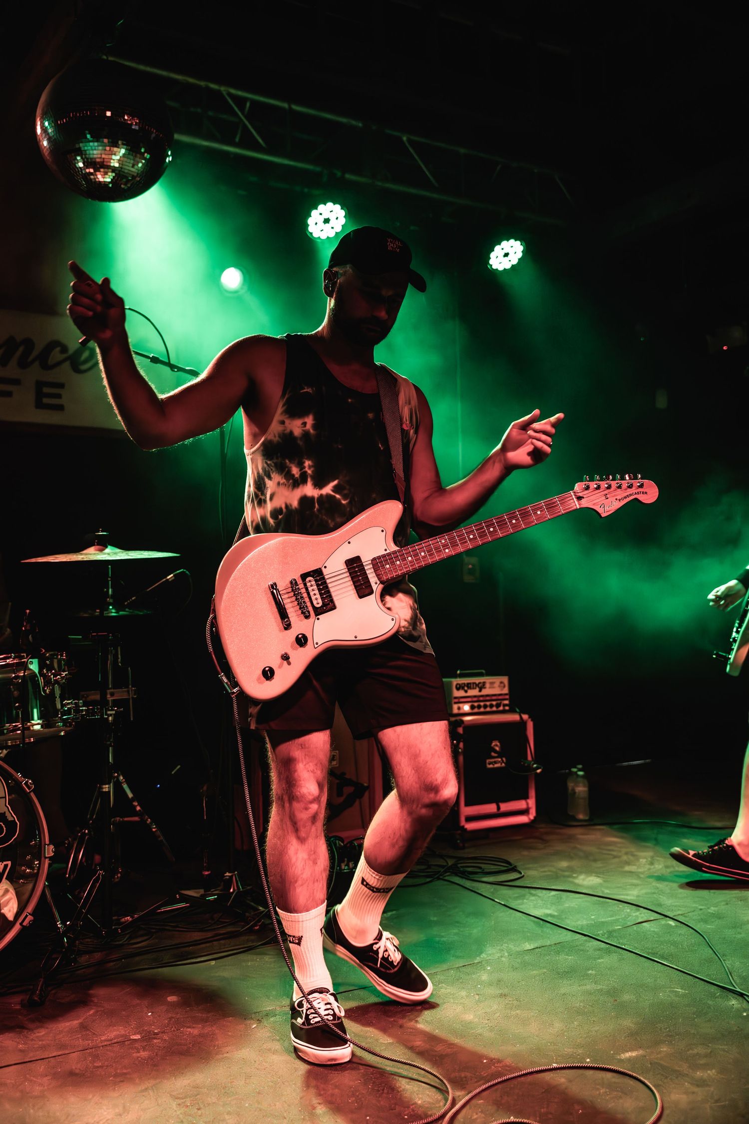 Musician plays electric guitar while jumping on stage under green spotlights.