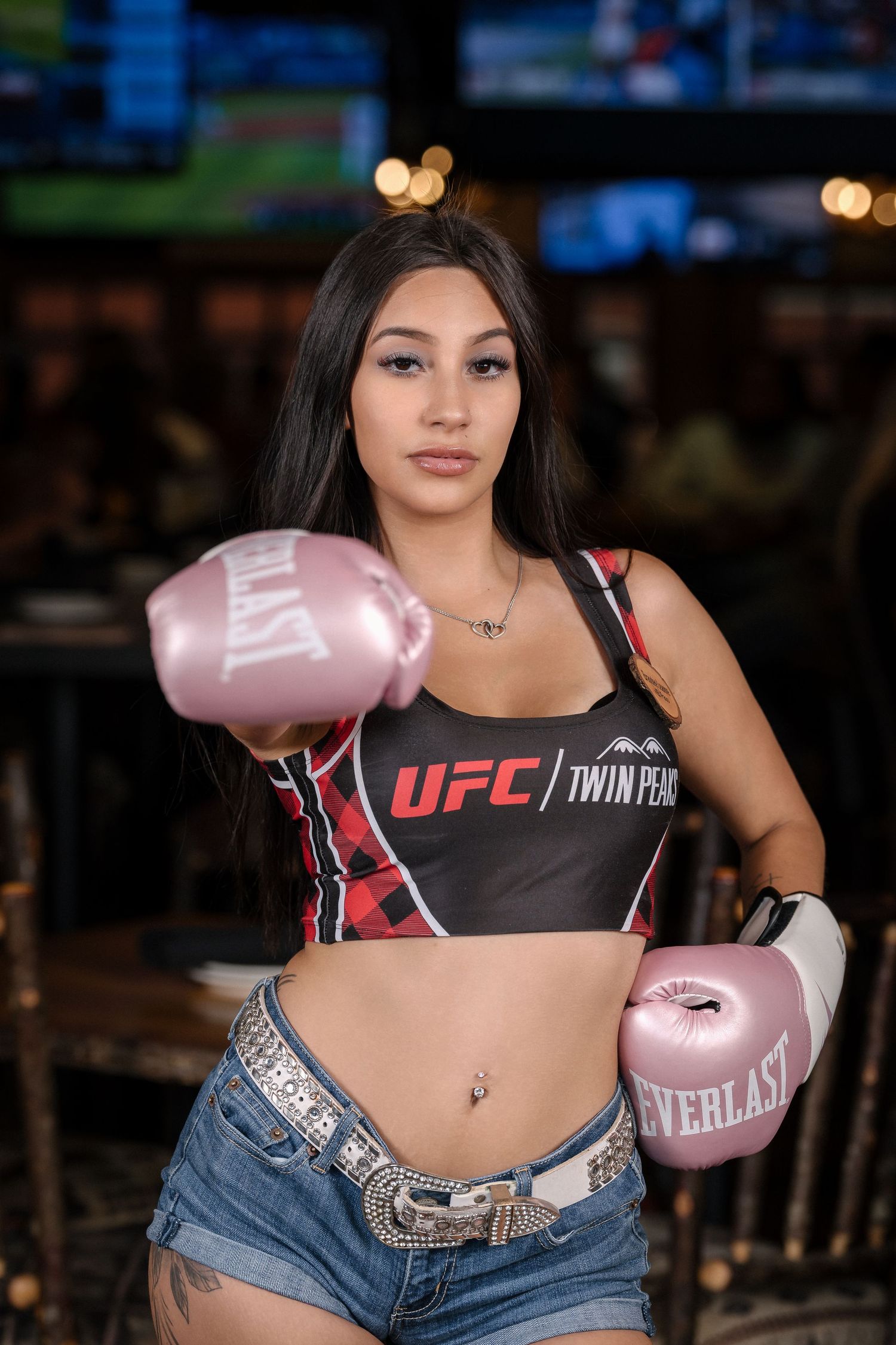 Model in UFC crop top and denim shorts poses with pink boxing gloves.